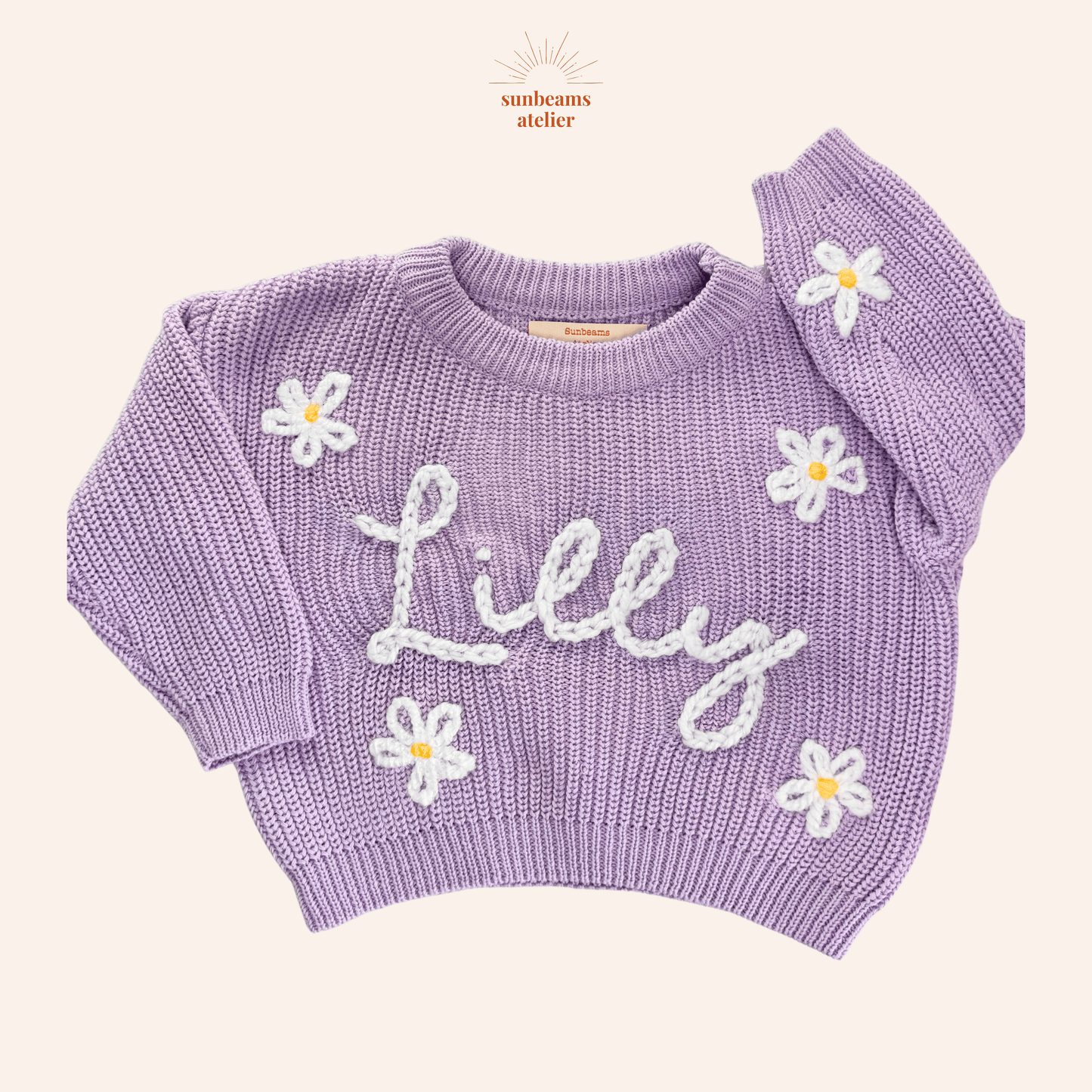 Strickpullover in der Farbe Lavender mit bestickten weiß-gelben Gänseblümchen und einem weißen bestickten Schriftzug "Lilly"