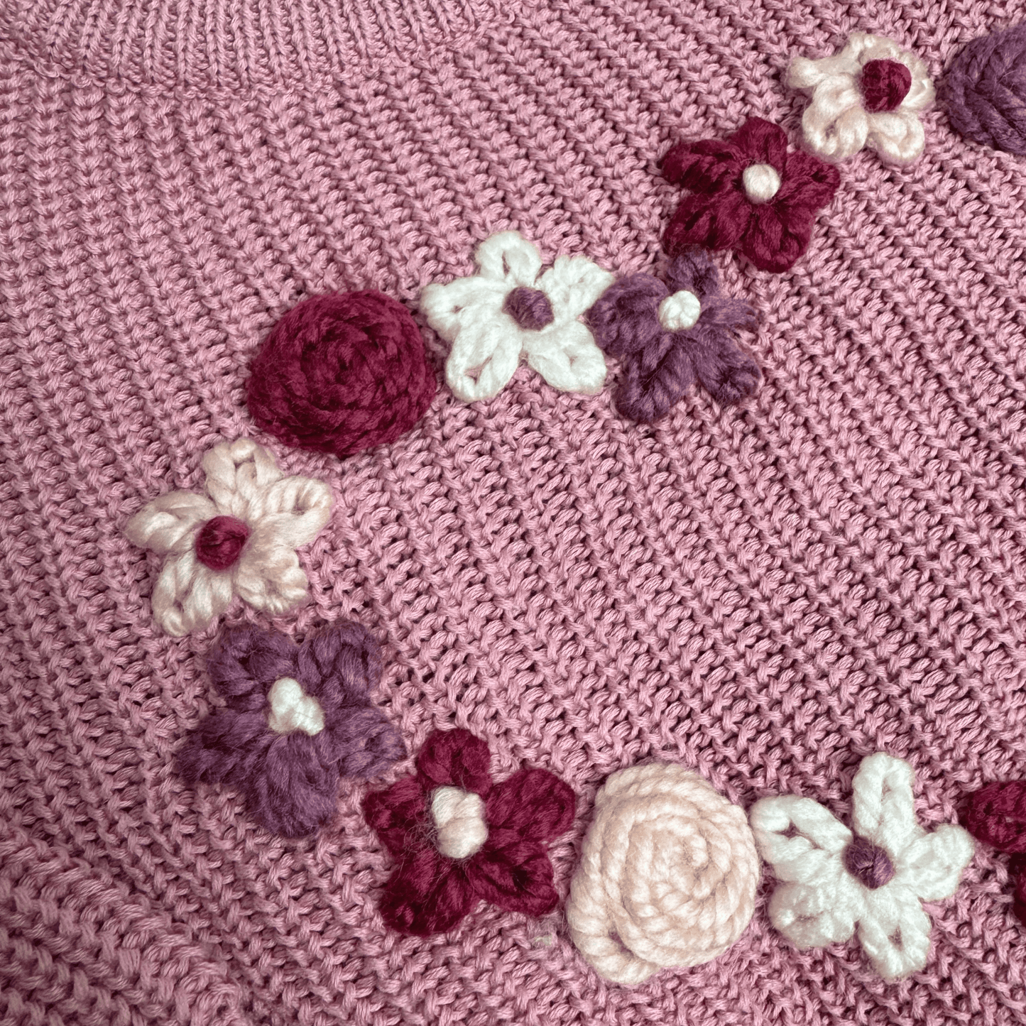 Detailansicht eines rosanen Pullovers mit vielen bestickten Blumen und Rosen in Rosa-Lila Tönen und weißen Details