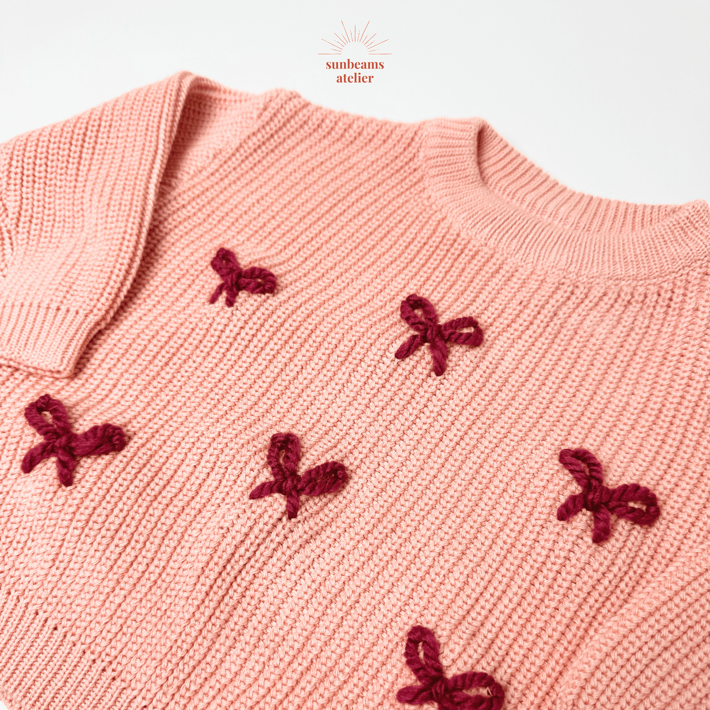 Rosa Pullover mit rot bestickten Schleifchen