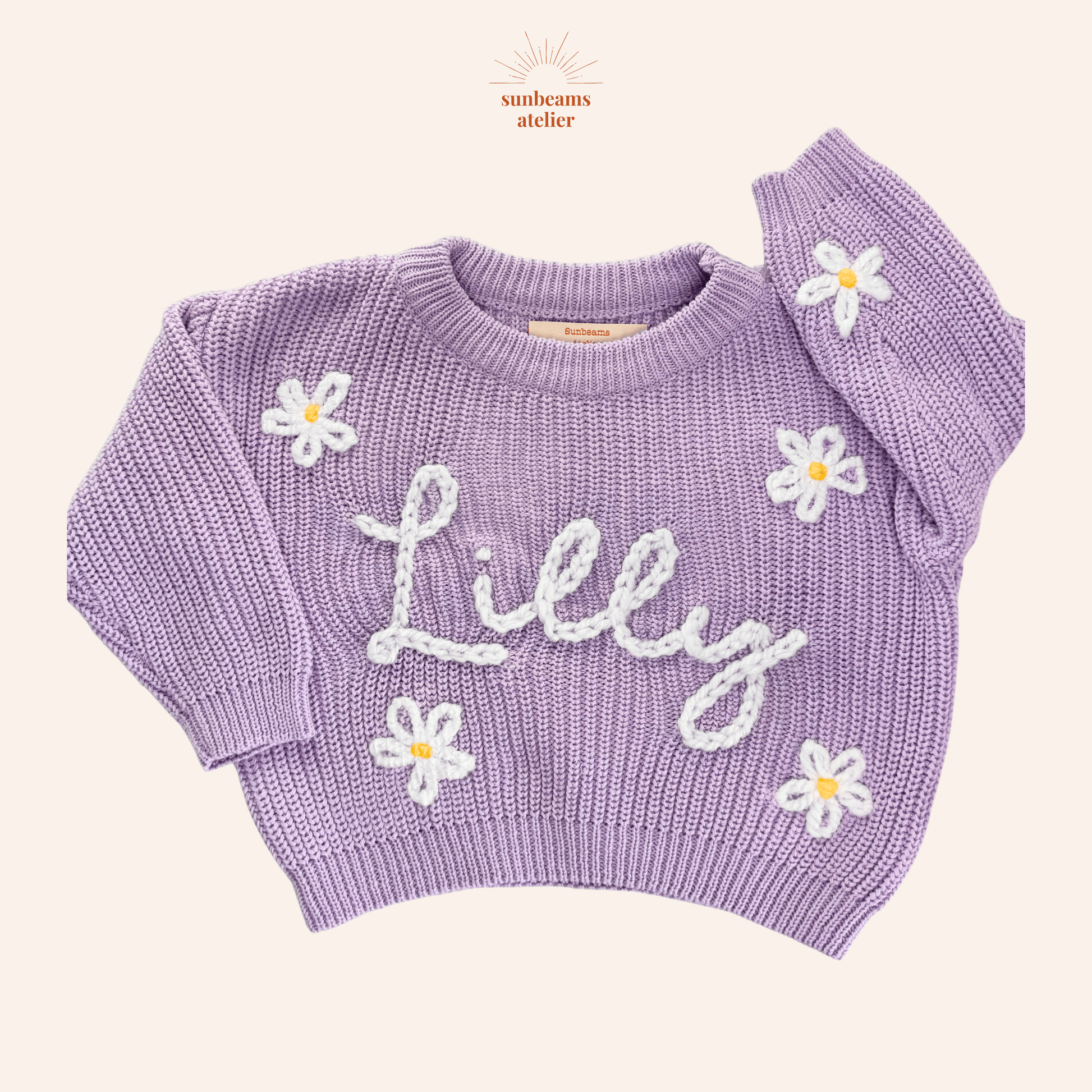 Strickpullover in der Farbe Lavender mit bestickten weiß-gelben Gänseblümchen und einem weißen bestickten Schriftzug "Lilly"