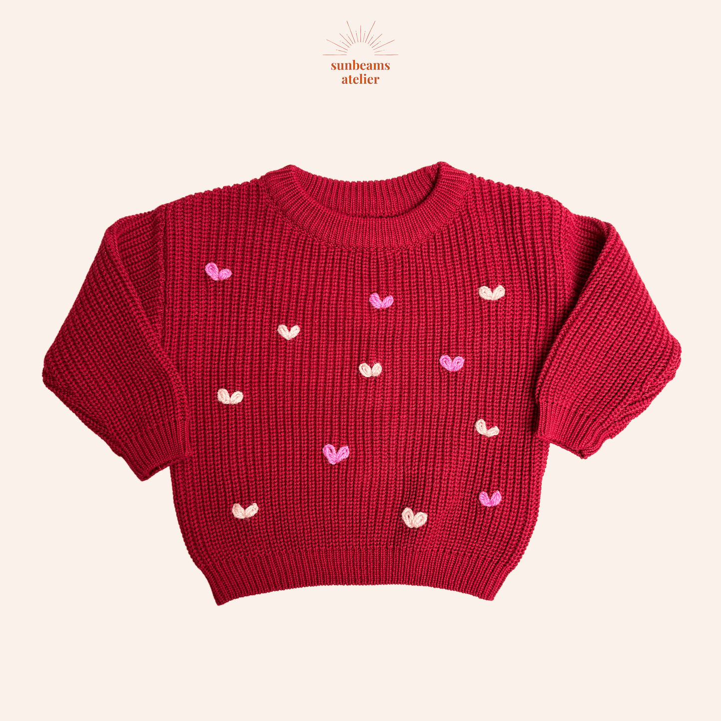 Produktbild mit einem roten Strickpullover und vielen kleinen rosa und hellen bestickten Herzchen mit regular Garn