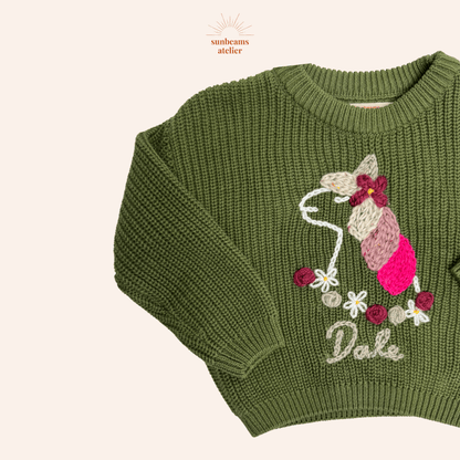 Strickpullover in green mit einem bestickten Einhorn und ein Blumenkranz aus Blüten und Rosen. Unten ist ein bestickter Schriftzug "Dale"