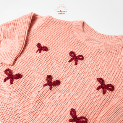 Rosa Pullover mit rot bestickten Schleifchen